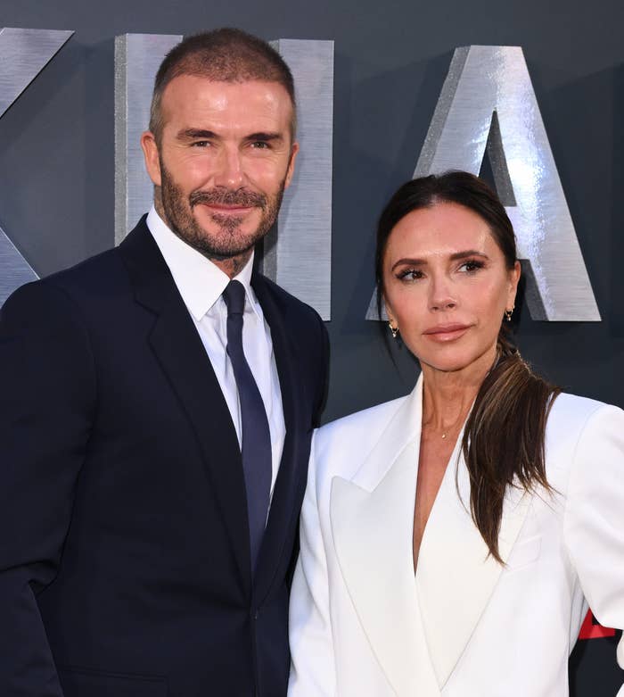 David Beckham and Victoria Beckham at a Netflix event, David in a suit and tie, Victoria in a tailored pantsuit with a clutch