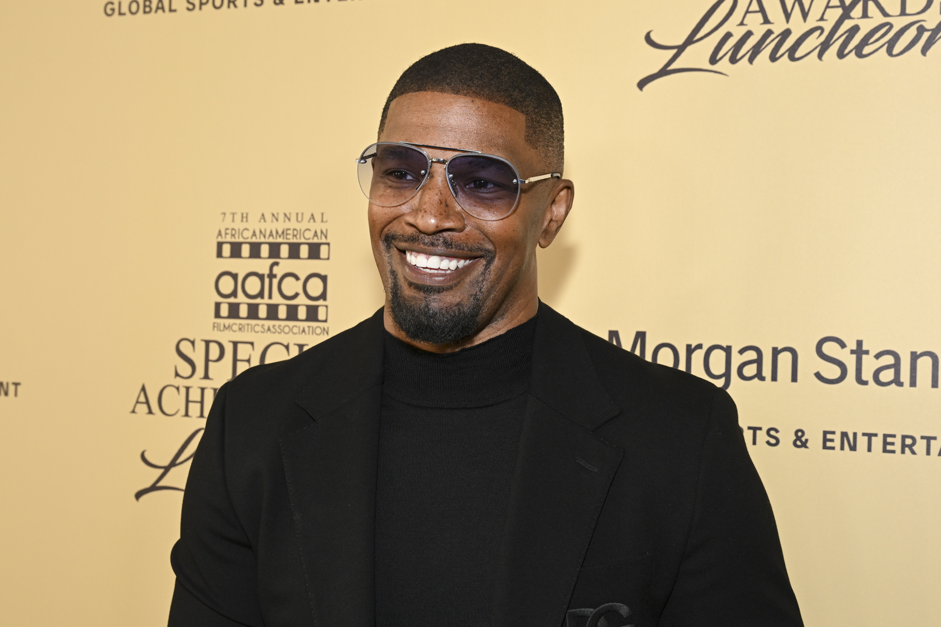 Jamie Foxx at the 7th Annual African American Film Critics Association Awards, wearing a black turtleneck and jacket with aviator sunglasses, smiling