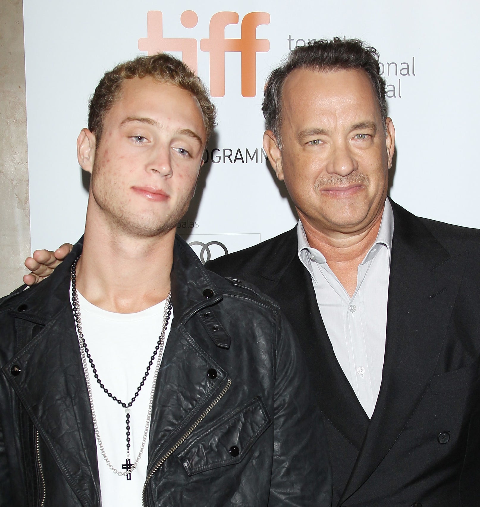 Tom Hanks and Chet Hanks pose together at a Toronto International Film Festival event. Chet is wearing a leather jacket, and Tom is in a suit