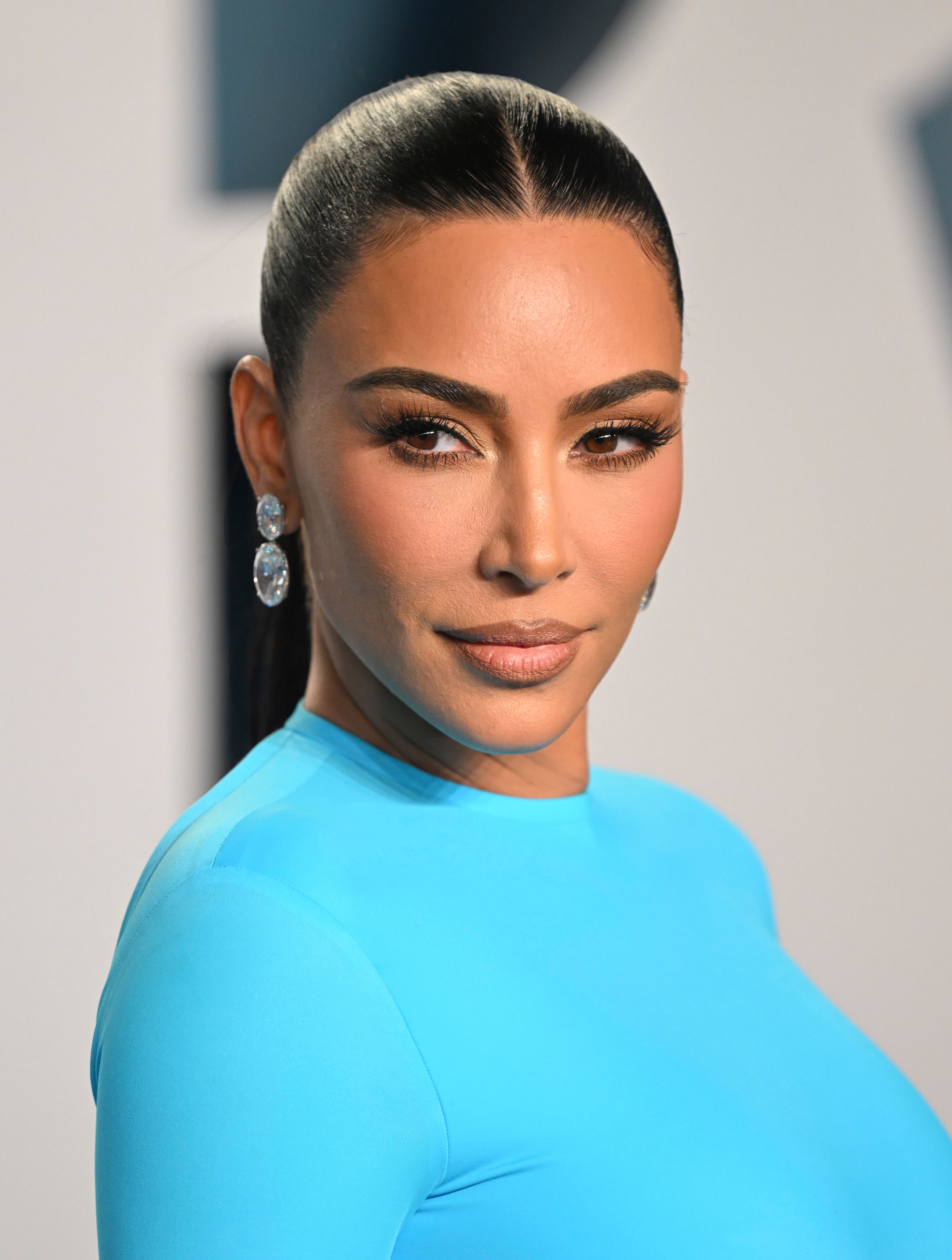 Kim Kardashian poses in a sleek, form-fitting outfit with elegant earrings at an event