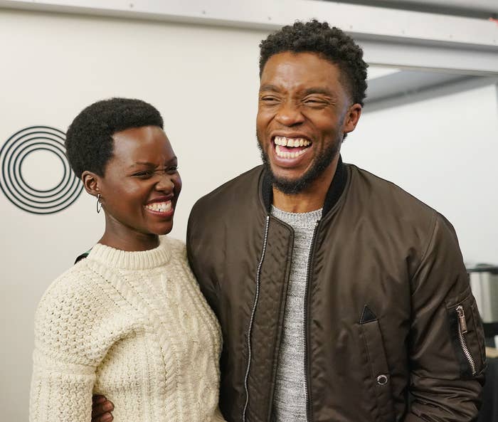 Lupita Nyong&#x27;o in a sweater and Chadwick Boseman in a jacket laughing together indoors