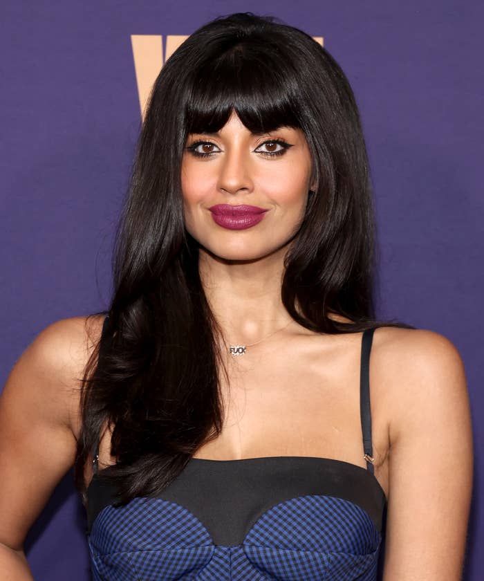 Jameela Jamil poses on the red carpet in a fitted, spaghetti-strap dress with a geometric pattern. She is wearing her hair down with bangs and minimal jewelry