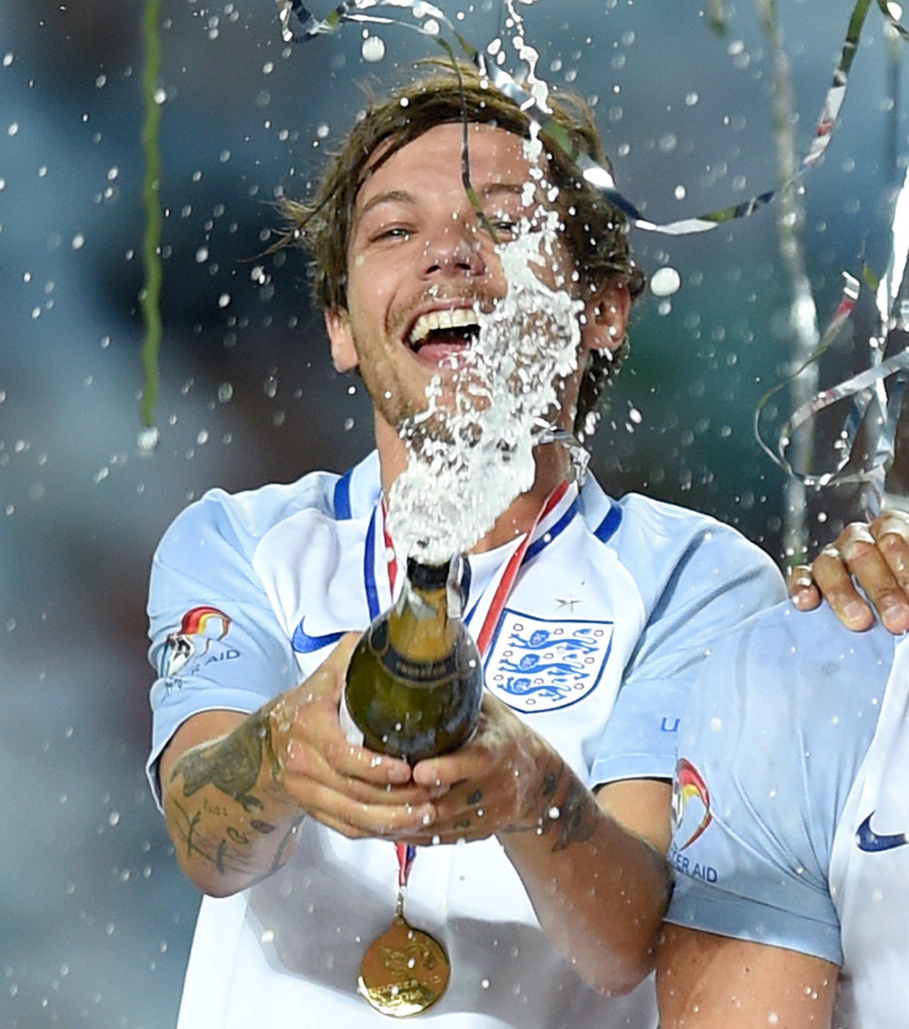 Louis Tomlinson celebratory sprays champagne while wearing a jersey and medal at a sports event