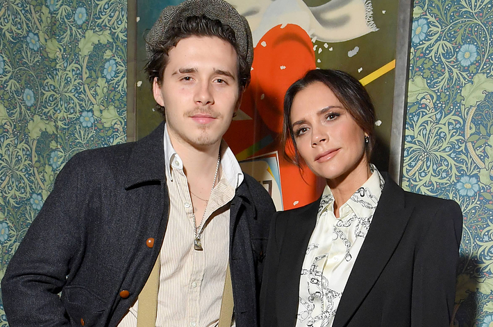 Brooklyn Beckham and Victoria Beckham pose together at an event, with both wearing stylish, semi-formal outfits