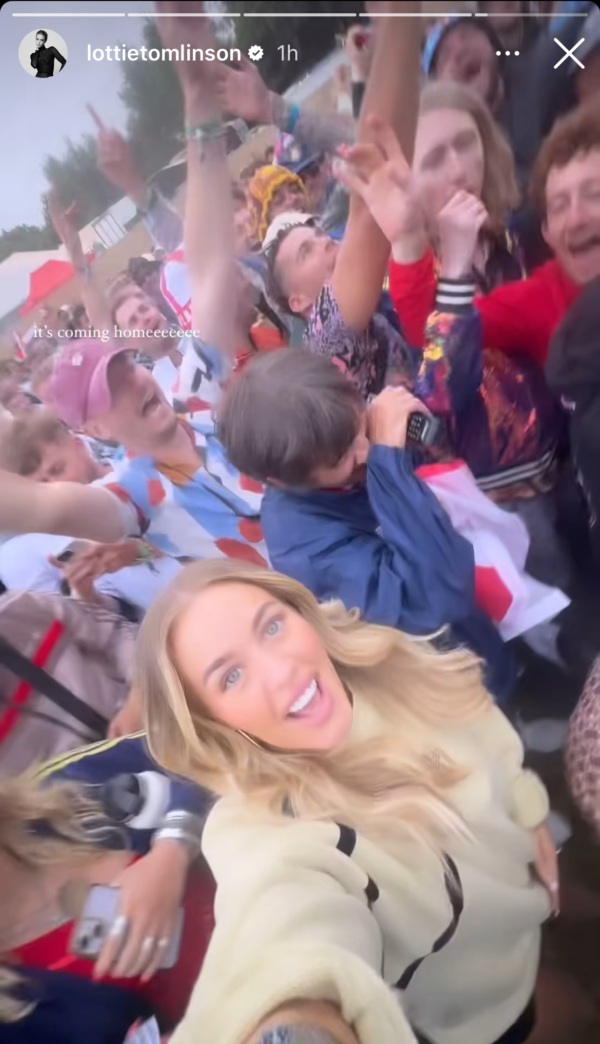 Lottie Tomlinson takes a selfie amidst a cheering crowd of England fans celebrating. She is dressed casually in a light-colored top